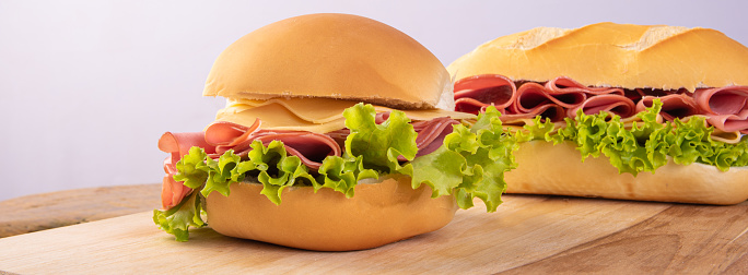 Mortadella, cheese and lettuce sandwiches on wooden surface, gray background, selective focus.