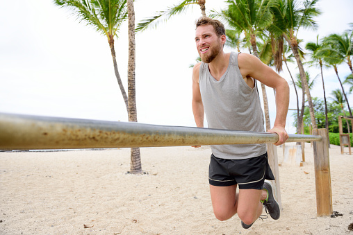 Bodyweight exercises man workout on dips bars. Male adult working out triceps and biceps on horizontal bars on beach as fitness training routine.