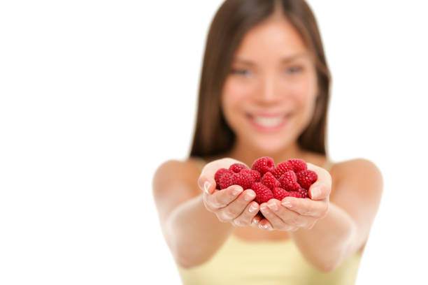 Woman holding fresh raspberries in hands closeup isolated on white background. Asian woman showing handful of red raspberries fruits in woman hands. Raspberry fruit berry healthy diet concept.