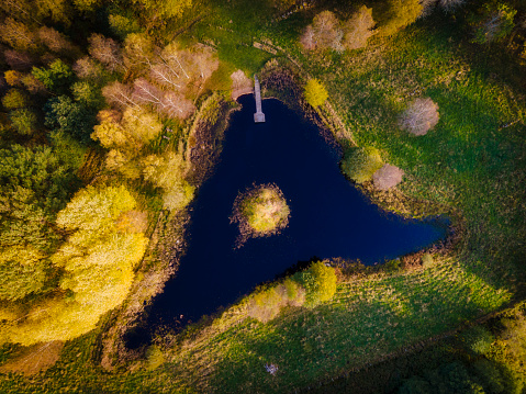 Small lake in woodland, forest, photographed from above,with a jetty, triangular