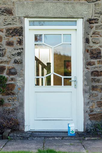 A front door of a residential building. There is a paper bag of prescription medicine outside it, it has been placed there for the homeowner to collect, to minimise contact during delivery.