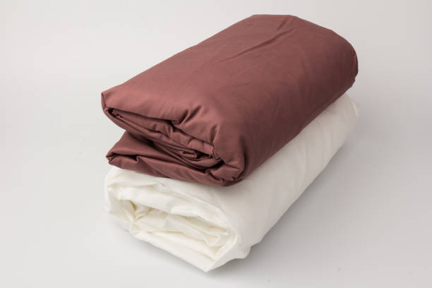 istock Stack of clean white and maroon bed sheets on white  background, closeup. 1281115719