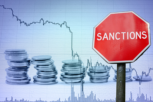 Sanctions sign against economy background with graph and coins.