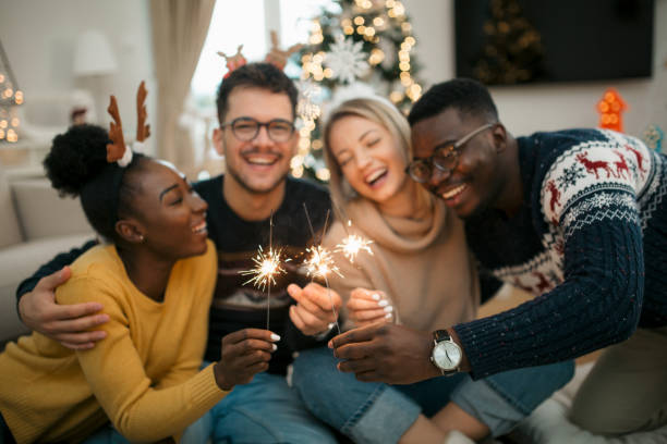 A small group portrait of people celebrating winter holidays with friends and family Portrait of a small diverse group of people celebrating Christmas at home, smiling, having fun and enjoying themselves and playing with sparklers christmas excitement stock pictures, royalty-free photos & images