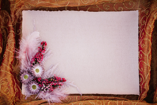 Empty rustic pink paper blank with dried boho flower arrangement framed by gold-coloured fabric with copy space