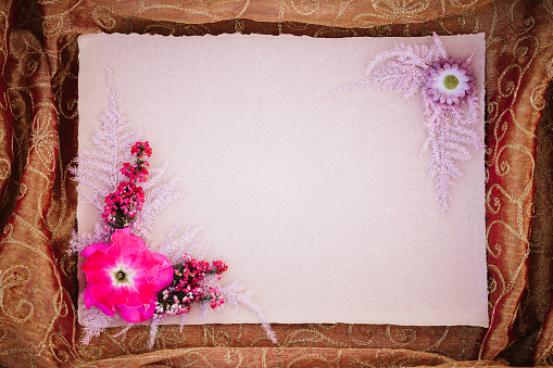 Empty rustic pink paper blank with boho flower arrangement framed by gold-coloured fabric with copyspace