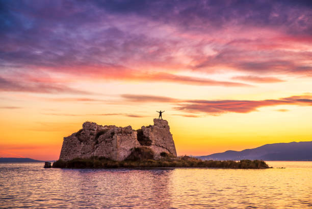 Freedom concept, unrecognisable man with raised hands at sunset over tower ruins in Delta del Ebro, Spain