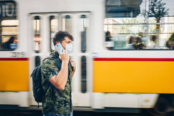 istock Young caucasian man with a protective face mask , talking on the phone in front of a moving tram. Outdoor photo. Coronavirus / air pollution/  traveling with public transport during coronavirus concept. 1281123778