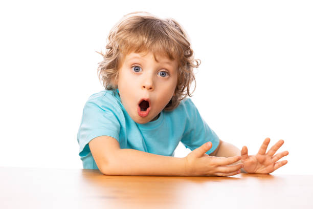 Portrait of four years old child sitting by the table. He is suprised