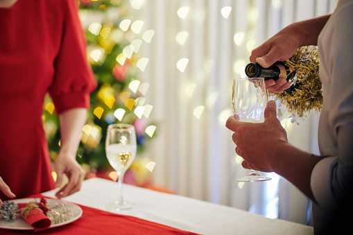 Man pouring champagne in flute when his wife decorating Christmas dinner table