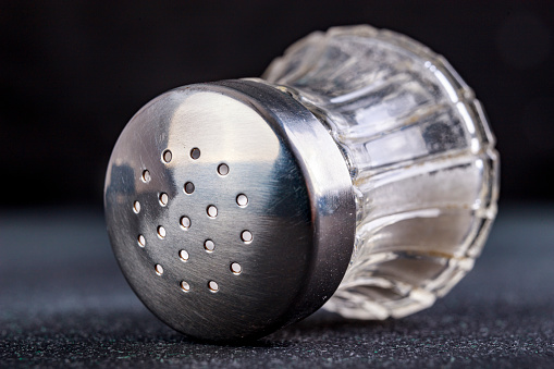 Glass salt shaker with metal cap, Kitchen accessories for seasoning dishes. Dark background.