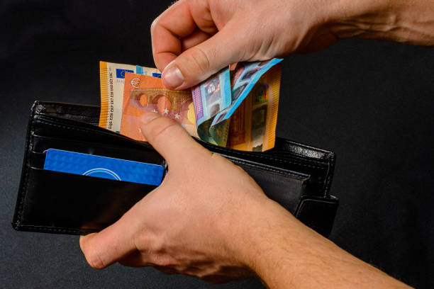 istock Man hand pulling money from wallet, black background and black wallet. 1281146455