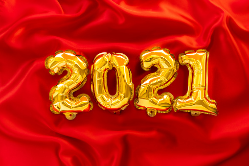 Foil balloons in the form of numbers 2021. New year celebration. Gold air balloons on red festive background. Holiday party decoration. top view