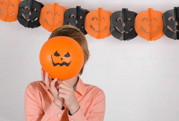 istock A boy hides his face behind an orange halloween balloon. 1281152505