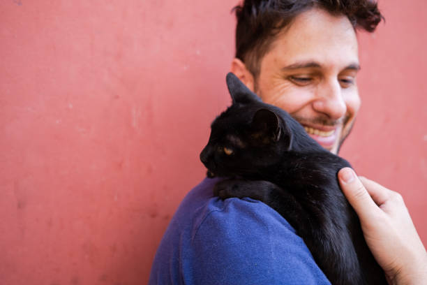 istock Man smiling holding a cute black cat on his shoulder 1281153856