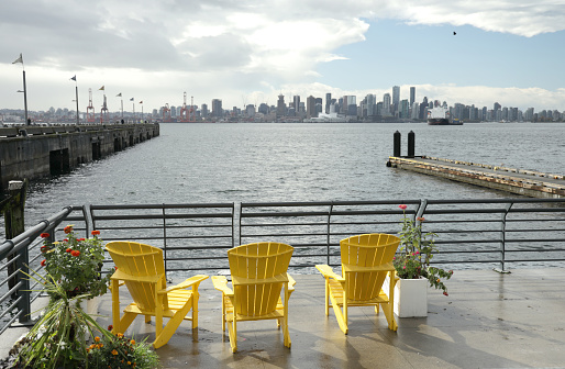 North Vancouver, Canada - October 13, 2020: Three yellow lawn chairs with a view from the Lower Lonsdale neighbourhood of North Vancouver to downtown Vancouver on an autumn afternoon.