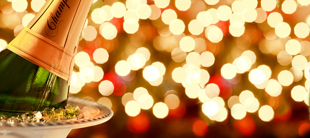 A bottle of holiday champagne in an ice bucket with a field of holiday lights in the background.