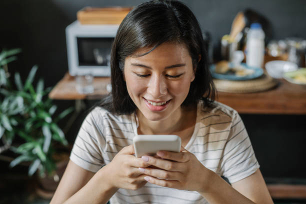 istock Happy Asian Woman Using her Smartphone While Sitting in the Kitchen in the Morning 1281156894