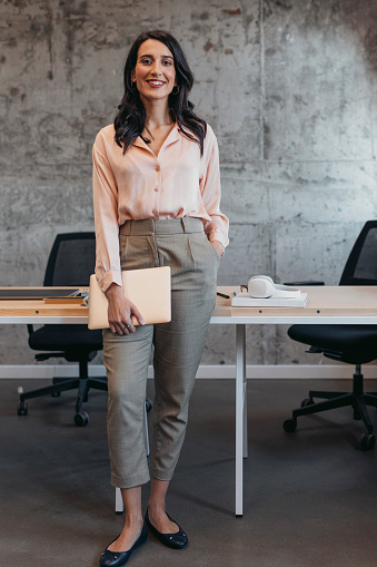 Indoor portrait of a smiling elegant businesswoman standing in her office holding a laptop computer.