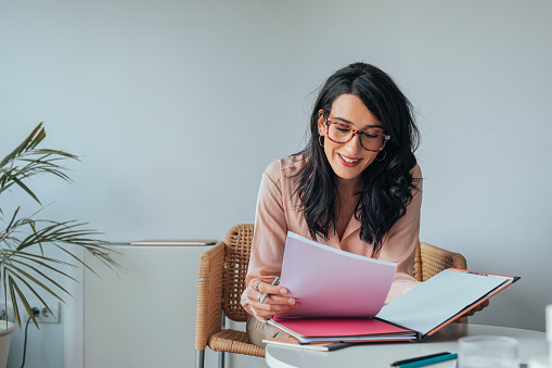 Smiling woman wearing glasses sitting in the office and doing paperwork.