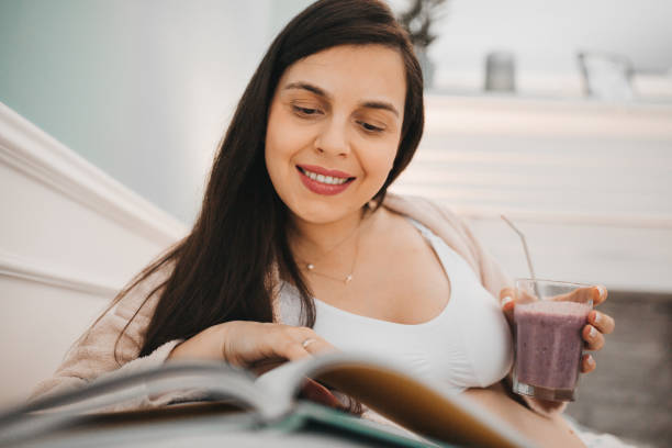 istock Pregnant woman reading book and drinking smoothie 1281166442