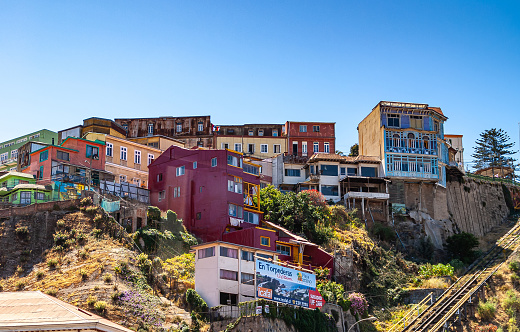 Valparaiso, Chile - December 8, 2008: Group of houses in different colors built on flank of hill under blue sky. Some green foliage,