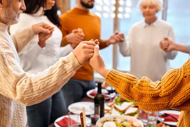 Close-up of mixed race family hands crossed other during prayer before holiday dinner at home. Christmas, New year, Thanksgiving, Anniversary, Hanukkah, Easter, Mothers day celebration concept