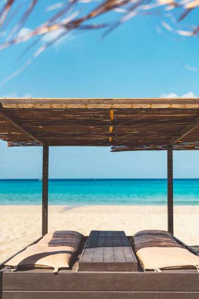 Vertical photo of sun bed for two on a sandy beach, Falassarna beach in Crete, Greece with a view of the ocean.