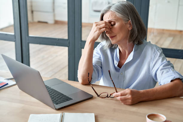 Overworked tired older lady holding glasses feeling headache, having eyesight problem after computer work. Stressed mature senior business woman suffering from fatigue rubbing dry eyes at workplace. mujer mayor cansada sobrecargada sosteniendo gafas que sienten dolor de cabeza, tener problemas de visión después del trabajo por computadora. mujer de negocios madura y estresada que sufre de fatiga frotando los ojos secos en el lugar de trabajo.
