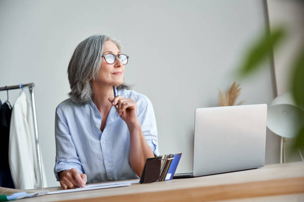 designer de mode femme mature aux cheveux gris idée de nouvelles idées créatives au travail. sourire belle élégante classe moyenne vieille dame propriétaire de petite entreprise rêvant dans le studio d’atelier. - pensive women business mature adult photos et images de collection