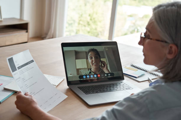 Old female hr reading cv during online job interview by video call. Senior employer checking indian seeker resume talking by social distance remote recruitment chat meeting videoconference on laptop. vieja mujer hr lectura cv durante la entrevista de trabajo en línea por videollamada. el empleador sénior que revisa al buscador indio reanuda la conversación por videoconferencia de videoconferencia de chat de reclutamiento remoto a distancia social en