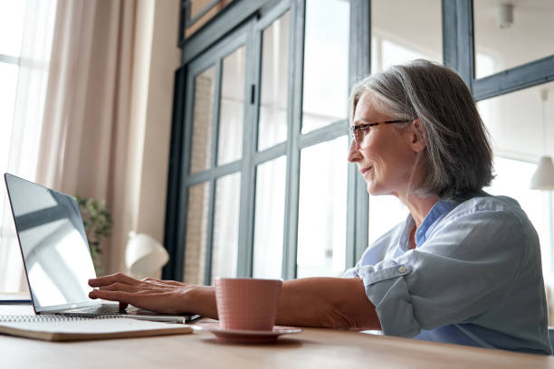 istock Smiling professional mature middle aged business woman using laptop computer sitting at workplace desk. Happy senior old lady 60s grey-haired businesswoman executive working on pc at home from office. 1281173454