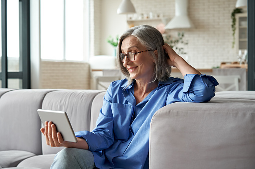 Feliz 60s mayor madura mediana edad mujer adulta sosteniendo tableta digital tableta de conferencia llamando por distancia social virtual familia reunión de chat en línea o viendo video sentado en el sofá en casa. photo