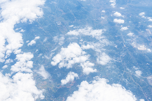 Aerial view from airplane window at high altitude of distant city covered with layer of thin misty smog and distant clouds.