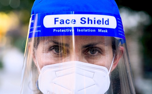 Caucasian pensive tired  Mature female healthcare worker looking at the camera wearing a n95 protective face mask and a face shield