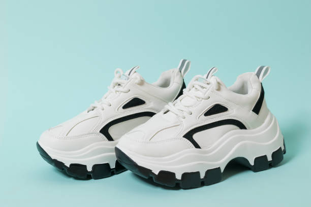istock Stylish white sneakers with black inserts on a blue background. 1281189052