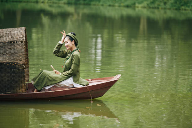 Scenic view of Vietnamese woman in traditional hat on wooden boat checking her fishing net on the Thu Bon River at Hoi An Ancient Town, Vietnam. Hoian is a popular tourist destination of Asia.