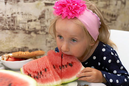 Girl bites a piece of red ripe watermelon