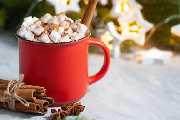 Beautiful christmas drink in the red cup with marshmallows and cinnamon with anis stars close-up. New year winter holiday celebration table. Festive decoraions