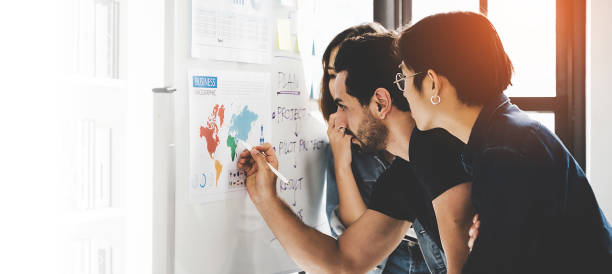 istock Business people meeting workshop at office and use post it notes to share idea. Brainstorming and teaching or coaching mentor concept. Paperwork document graph and diagram on whiteboard or flip chart 1281207817