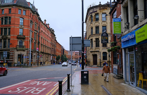 Manchester / United Kingdom - October 17, 2020. Empty streets of Greater Manchester during pandemic.  Only one man in viral mask approaching the camera. Taken during the rainy day.