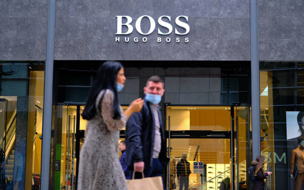 New Cathedral street in Manchester, England, with Hugo Boss shop front. Blurred unrecognisable young couple in face masks passing by it. stock photo