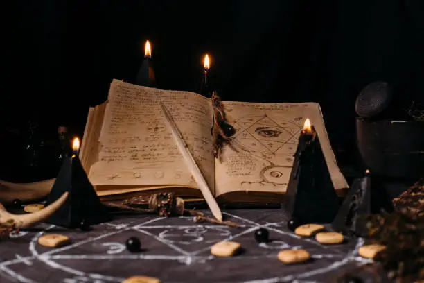 Open old book with magic spells, runes, black candles on witch table. Occult, esoteric, divination and wicca concept. Halloween vintage background