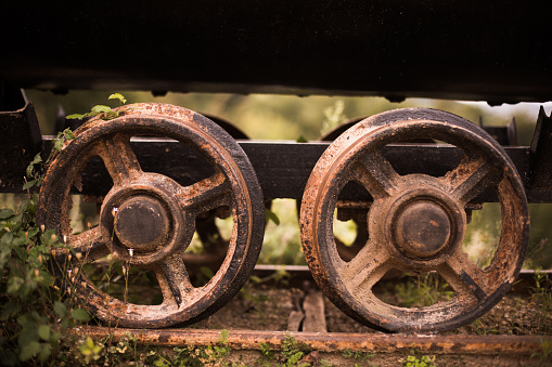 Close up shot of the rusty metal wheels of an abandoned wagon, with some plants growing.