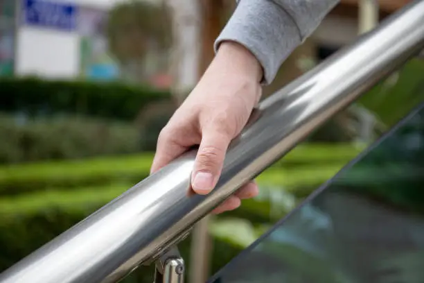 Photo of male hand holds metal handrail in a public place