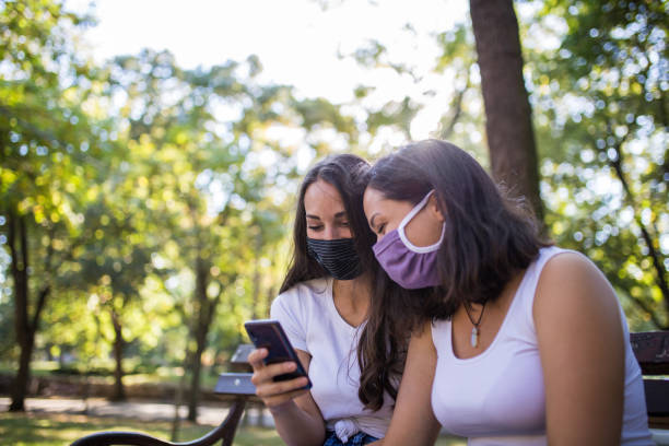 istock Two young beautiful friends seating on a bench in a park and using mobile phone 1281213279