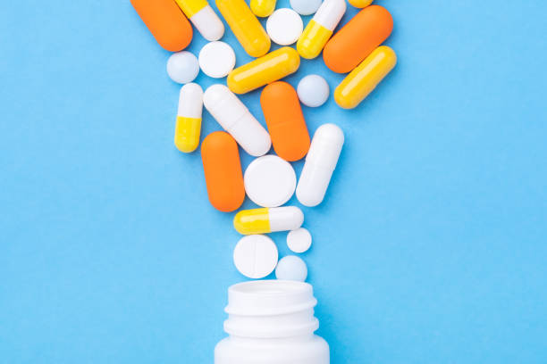 istock Multicolor tablets and pills capsules from plastic bottle on blue background Close-up 1281214417