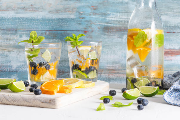 cocktails sains d’été d’eaux infusées d’agrumes, de limonades ou de mojitos, avec des bleuets orange citron lime et de la menthe, boissons de désintoxication diététique, dans des verres sur fond léger - lime fruit citrus fruit portion photos et images de collection