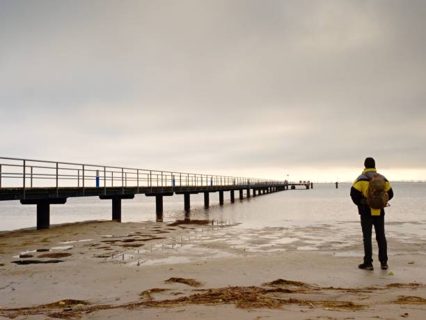 istock Man Hiker With Backpack Stand Alone On Dirty Sandy Beach And Watching Romantic Colorful Sunrise Sea 1281217386