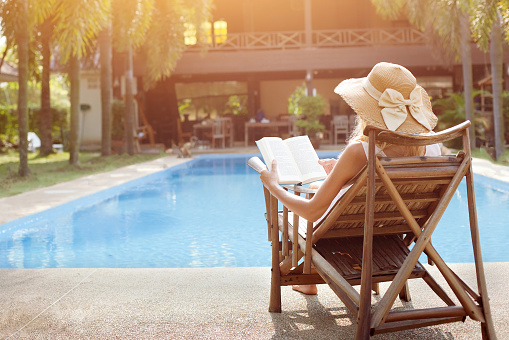 relaxation concept, woman reading book near swimming pool of hotel